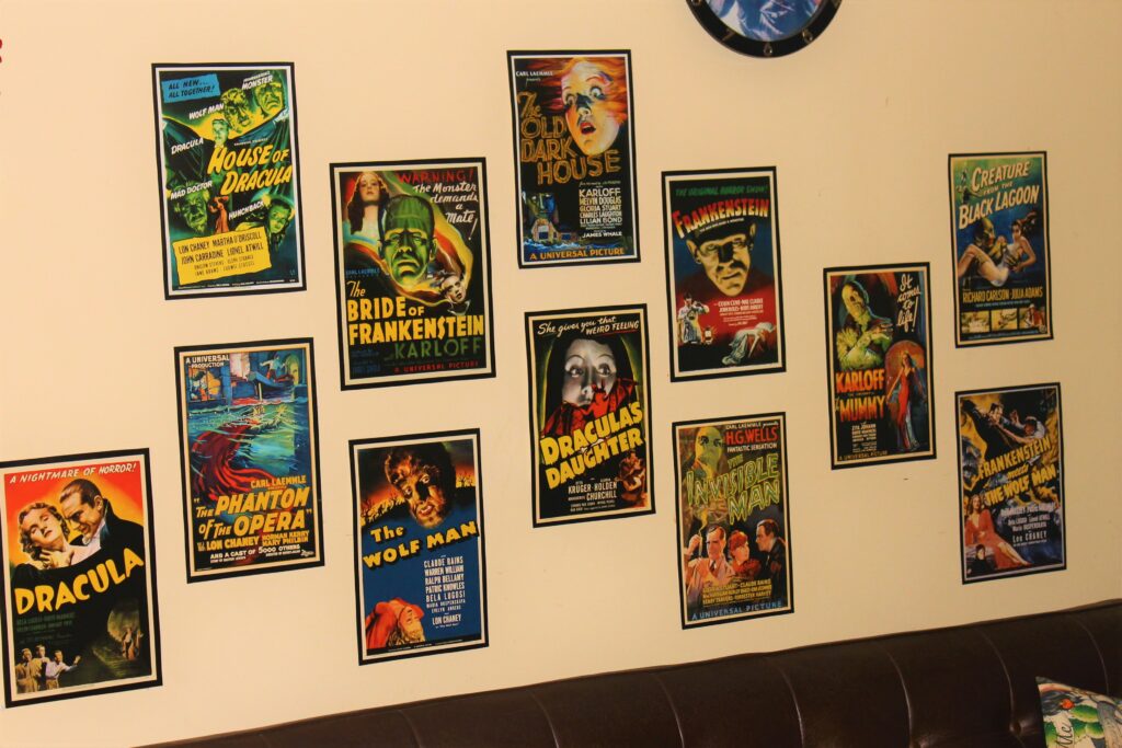 Image shows a sandy coloured wall covered in vintage horror movie posters taken from an expired calendar. The posters are staggered somewhat randomly.