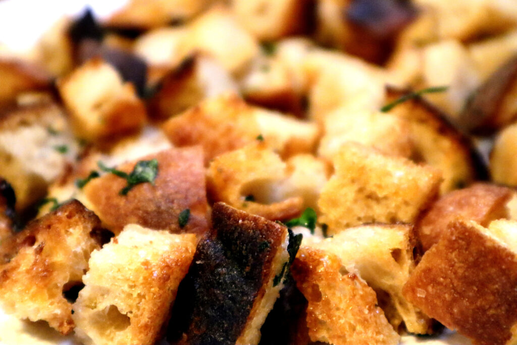 Closeup of Crunchy Herbed Croutons. They are crispy golden cubes of fried bread, sprinkled with green herbs.