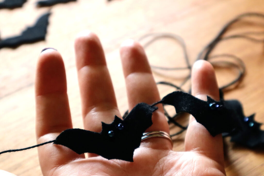 Closeup of Maddy the Maker's hand holding the felt bat garland. Maddy is wearing dark bergundy nailpolish.