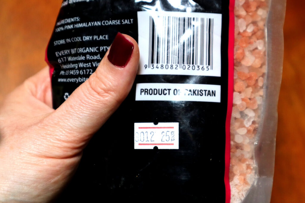 Image shows Maddy the Maker's hand, holding a packet of Pink Himalayan Rock Salt. Maddy is wearing dark bergundy nailpolish. The back of the packet is visible, showing text, a barcode, and and expiry date which reads "25 EXP".