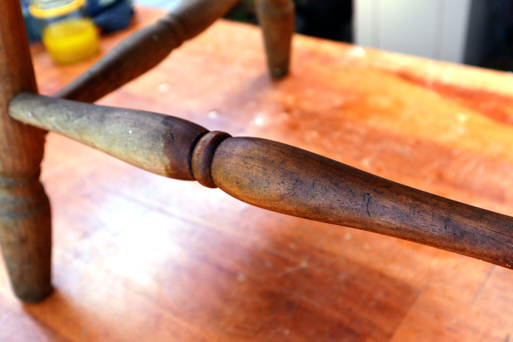 Detail of a vintage timber chair. Eco friendly wood polish has been applied to one part, here the wood looks clean and hydrated. Another section has not had the wood polish applied, here it looks dry and dirty. The chair is shown on a timber surface.