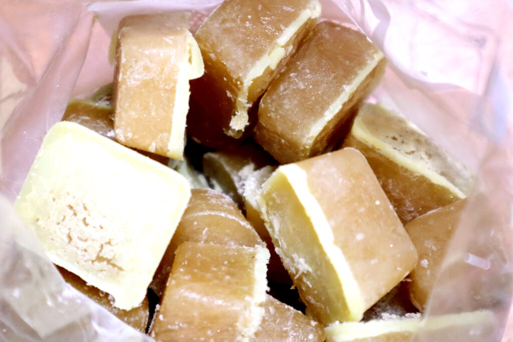 Image shows an open plastic bag full of golden coloured homemade chicken stock ice blocks. The top of each ice block is covered in a thick coating of pale yellow fat.