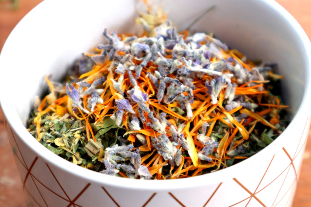 Nervous/Immune System HealingTea is shown in a white ceramic canister with copper coloured geometric patterning. The ingredients have been added to the jar but have not been mixed together. The top layer is bright orange and purple from calendula and lavender petals.