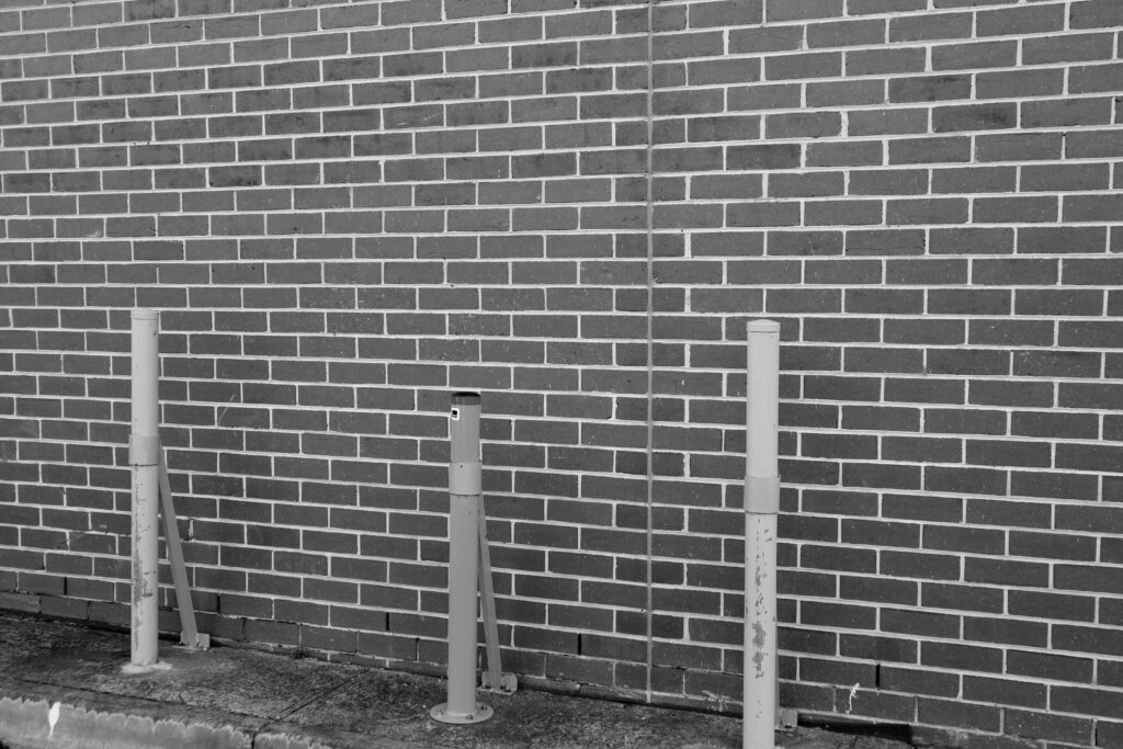 Black and white image of a brick wall protected by bollards. The image represents strong boundaries.