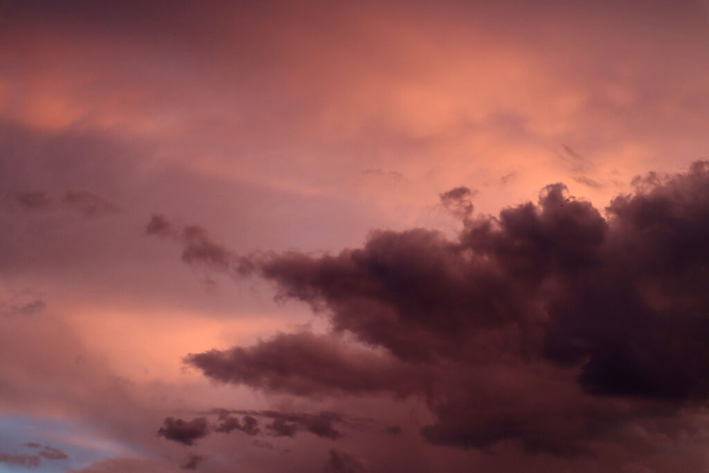 Storm clouds at sunset. The sky is varying shades of pink. There is an ominous dark shadowy storm cloud across the bottom right of the picture. The dark clouds are used to represent shadow work.