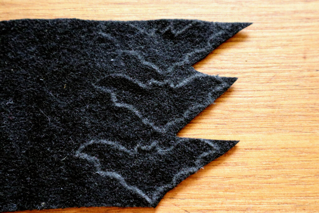 Image shows a piece of black felt with three bat shapes outlined in white chalk pencil. The felt is shown on a vintage timber desk.